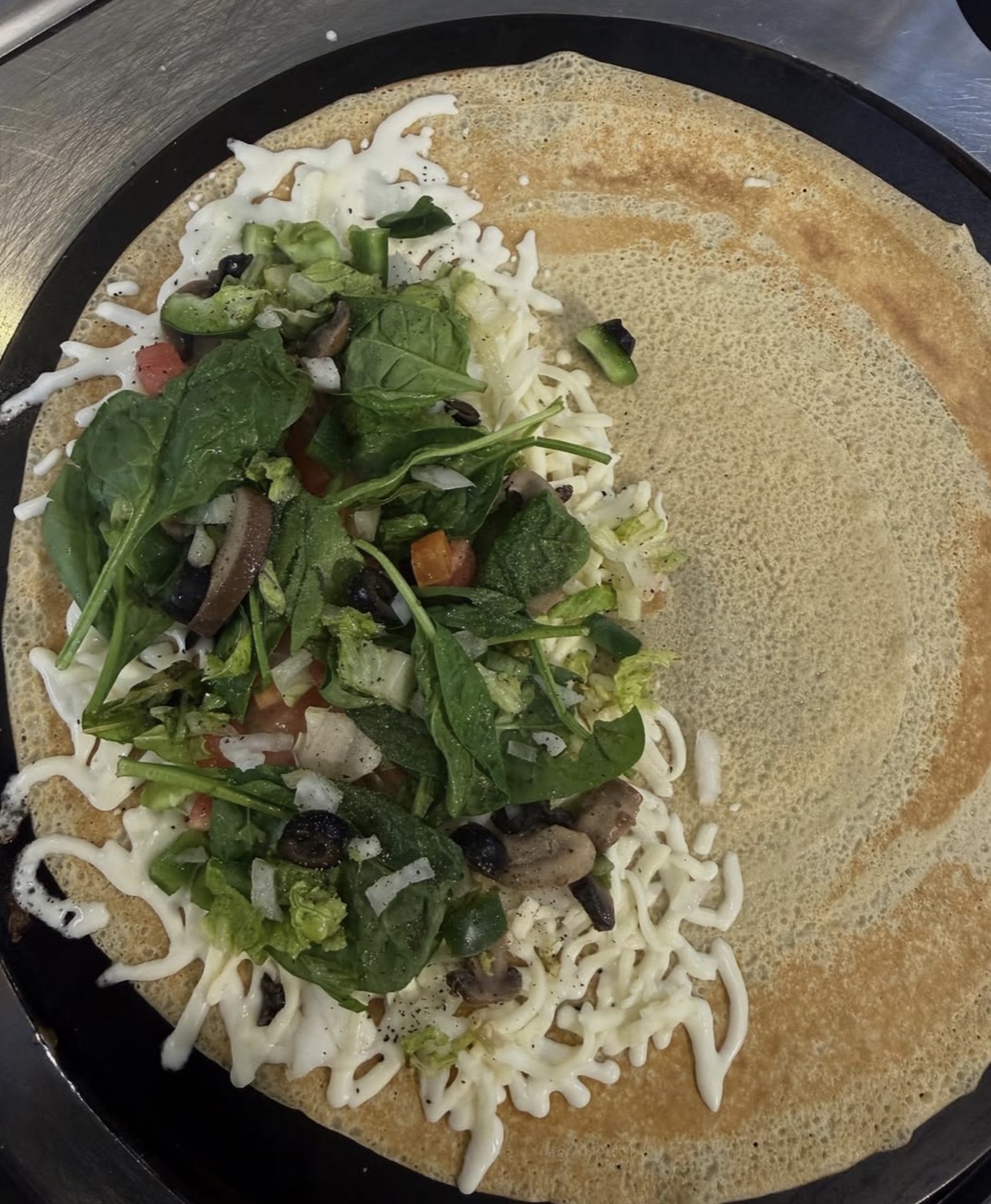 Veggie crepe loaded with spinach, olives, tomato and melted cheese